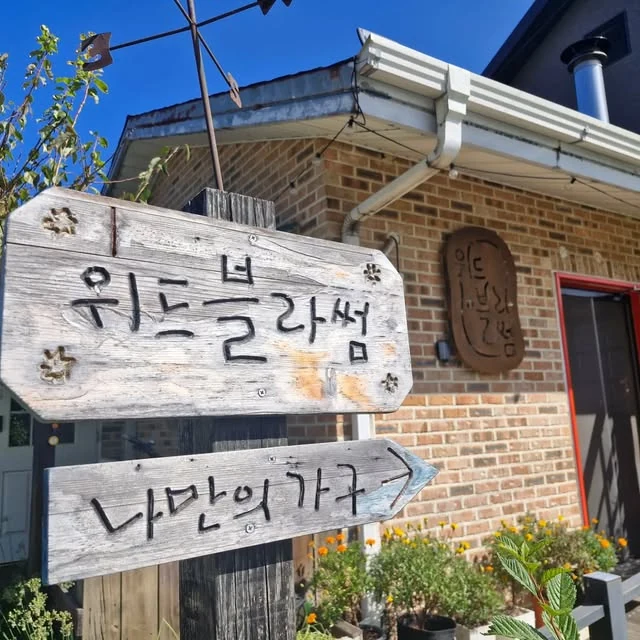 위드블라썸 나만의 아지트라고 적힌 나무 간판과 벽돌집